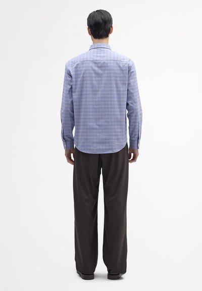 Niebiesko-fioletowa kraciasta koszula z długim rękawem, kołnierzykiem na guziki, zaokrąglonym dołem i gładką fakturą materiału. Nosi się ją z szerokimi brązowymi spodniami.