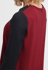 Maglia a maniche lunghe con parte anteriore bordeaux e maniche blu navy, tessuto testurizzato e dettaglio con bottone a chiave sul retro.