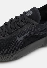 Sort Nike-sneaker med en struktureret mesh-overdel, flade snørebånd og en glat sål med et prikket mønster. Inkluderer en subtil logo-detalje.