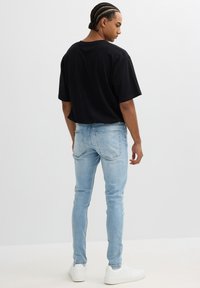 Camiseta negra de manga corta combinada con jeans ajustados de color azul claro y zapatillas blancas. Tejido suave con un diseño minimalista, sin patrones visibles.