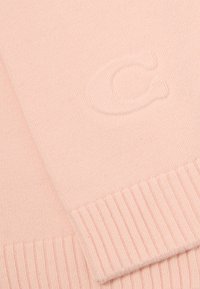 Écharpe en tricot rose clair avec un ourlet côtelé et un détail de logo en relief. Le tissu a une texture lisse avec un motif de tricot fin.