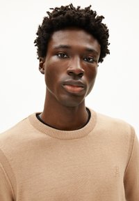 Beige Pullover mit Rundhalsausschnitt und geripptem Kragen. Verfügt über eine glatte Strickstruktur und ein dezentes Logodetail auf der Brust.