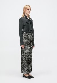 Blusa nera con scollo a fiocco abbinata a una lunga gonna decorata con paillettes in un gradiente di argento e nero. Ballerine nere completano il look.