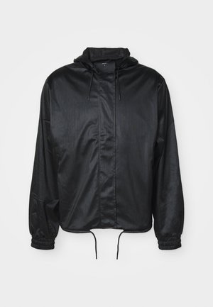 Casaco preto com capuz feito de tecido liso e leve. Apresenta punhos elásticos, bainha ajustável com cordão e fecho zip na frente.