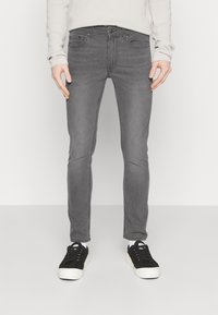 Jeans ajustados grises con una textura suave, diseño de cinco bolsillos y un ligero desgastado. Combinados con zapatillas negras y calcetines blancos.