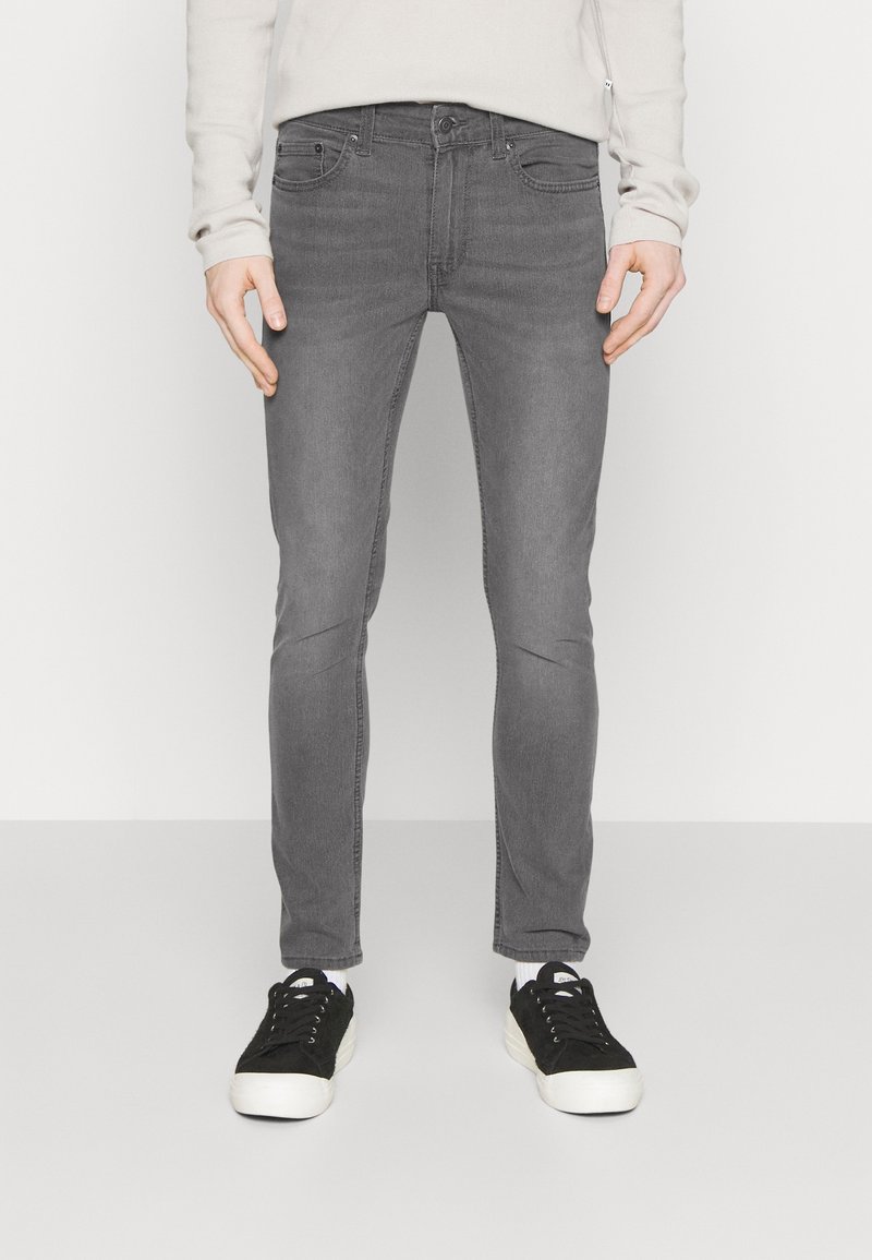 Jeans ajustados grises con una textura suave, diseño de cinco bolsillos y un ligero desgastado. Combinados con zapatillas negras y calcetines blancos.