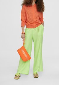 Bright orange zip-up hoodie with ribbed texture, paired with loose-fitting, light green pants. Accessories include orange bag and sandals.