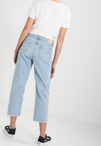 Ljust blå denimjeans med rak benmodell, rå kant och två bakfickor. Matchas med en vit kortärmad skjorta och svarta sneakers.