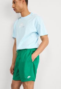 Svetlo modré tričko Nike s krátkymi rukávmi a bielym logom; zelené šortky Nike s elastickým pásom a vreckami.