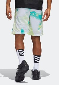 Pantalones cortos atléticos de malla con una base blanca y un patrón de salpicaduras en verde-azul, combinados con zapatos negros y calcetines de rayas en blanco y negro.