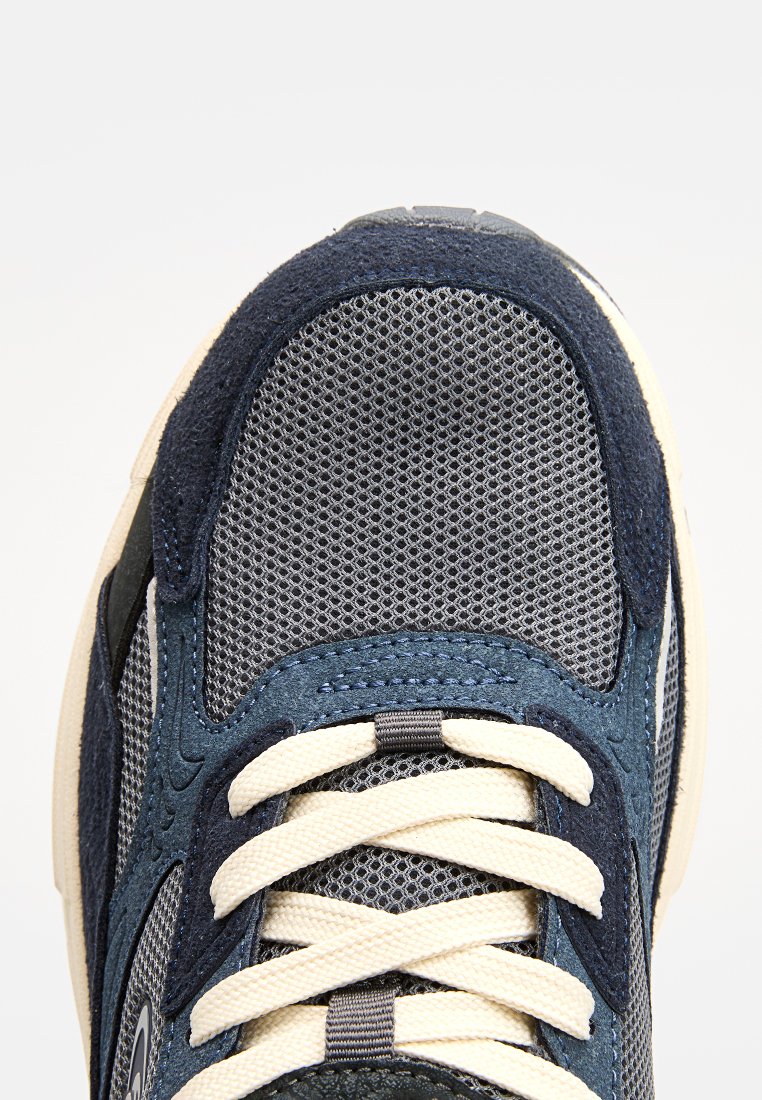 Herren Sneaker mit einem grauen Mesh-Obermaterial und Akzenten aus marineblauem Wildleder, cremefarbenen Schnürsenkeln und einer strukturierten, weißen Gummisohle.
