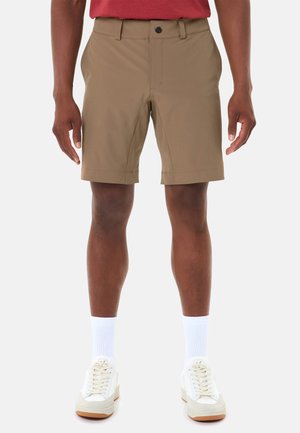 Mann, der khakifarbene Shorts, weiße Sportsocken und weiße Turnschuhe trägt, steht mit locker an den Seiten hängenden Armen.