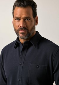 Granatowa koszula z guzikami, wykonana z teksturowanej tkaniny, z wyraźnym kołnierzykiem i kieszenią na piersi z zapięciem na guzik.