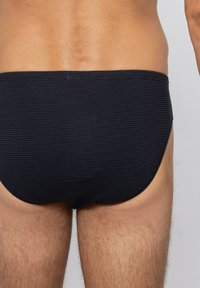 Svarta simbrallor med ett horisontellt randmönster, med en låg sittande design och mjukt tyg som formas efter kroppen.