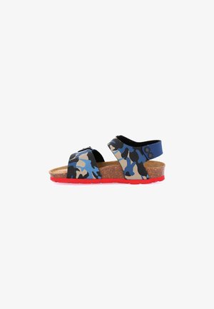Sandalo per bambino con cinturini camouflage blu, neri e beige, sottopiede in sughero e suola rossa, su sfondo bianco.