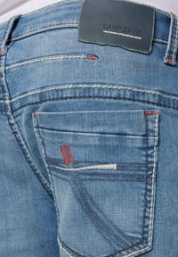 Hellblaue Denim-Jeans mit einem Lederpatch auf der Rückseite, auffälligen roten und weißen Nähdetails sowie einem klassischen Fünf-Taschen-Design.