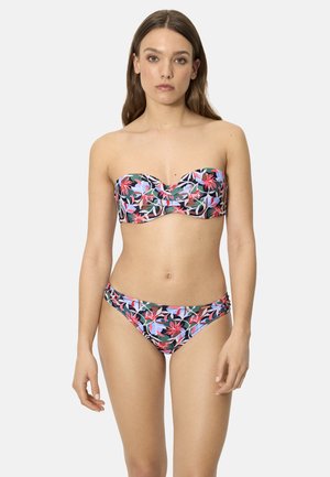 Mujer con bikini sin tirantes de estampado floral multicolor, de pie frente a un fondo claro y liso, mirando al frente con expresión neutral.