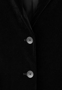 Primo piano di un blazer in velluto nero con due bottoni argentati lucidi chiusi sulla parte anteriore.