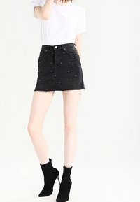 Svart jeansminikjol med osydd kant, dekorerad med silvernitar fram, kombinerad med en vit t-shirt och svarta ankelstövlar.