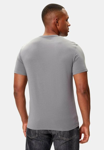 Szara koszulka z krótkim rękawem z okrągłym dekoltem, gładką fakturą i dopasowanym krojem, zestawiona z ciemnymi jeansami.