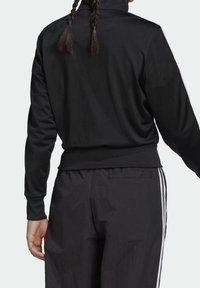 Svart sportjacka med hög krage och långa ärmar. Mjukt tyg, figursydd midja, kombinerad med lösa svarta träningsbyxor med sidostripe.