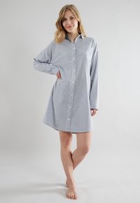 Abito a righe blu e bianco con bottoni. Presenta maniche lunghe, una tasca sul petto e una vestibilità morbida che arriva sopra il ginocchio.