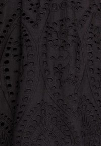 Tela negra con patrones de cachemira bordados, que presenta detalles recortados y costuras texturizadas, creando un efecto visual en capas.