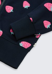 Manche de sweat-shirt bleu marine avec motifs fraises roses et détail de bord-côte côtelé, montrant une partie d'une fermeture éclair avant et un ourlet.