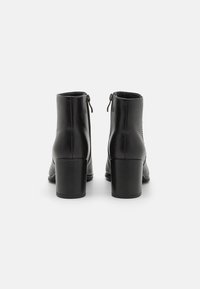 Botas de cuero negro hasta el tobillo con punta redonda, cierre de cremallera y tacón alto y grueso. La textura suave presenta detalles de costura sutiles.