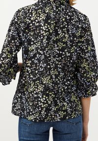 Blusa nera floreale con maniche a sbuffo, caratterizzata da un motivo colorato di fiori e forme geometriche. Tessuto morbido con una vestibilità comoda.