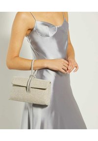 Sprankelende zilveren clutch met een omslagflap en een gestructureerde afwerking. Voorzien van een decoratieve lus handvat. Draagt bij een satijnen zilveren jurk.