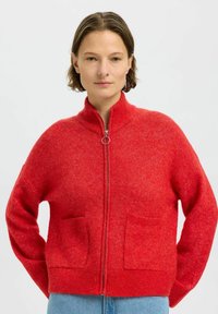 Rode wolmix cardigan met een hoge kraag, ritsafsluiting en twee voorzakken. Zachte textuur en een relaxte pasvorm.