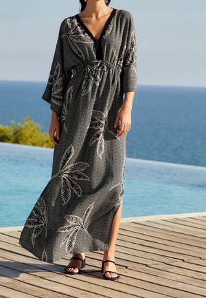 Vestido largo negro con estampado de hojas de palma blancas, con escote en V, mangas oversized y cintura elástica, combinado con sandalias negras.