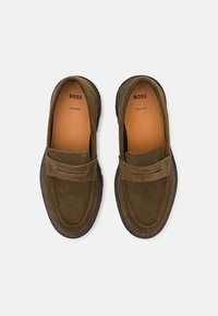 Pair of olive green suede loafers with stitched detailing, leather insoles branded "BOSS," and dark brown outsoles on a white background.