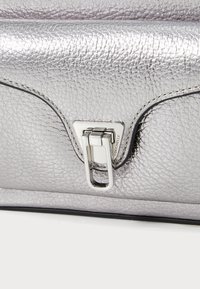 Zilveren leren handtas met een gestructureerd oppervlak, een rechthoekige vorm en een opvallende metalen sluiting met gegraveerde merkinformatie.