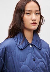 Ναυτικό γεωμετρικό μπουφάν με μεγάλο γιακά, που διαθέτει κυματοειδή ραφή, κλείσιμο με κουμπιά και λείο ύφασμα.