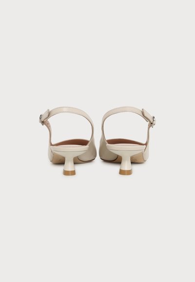 Paire de chaussures beiges à talons bas avec brides à la cheville et boucles, vue de dos sur fond blanc uni.