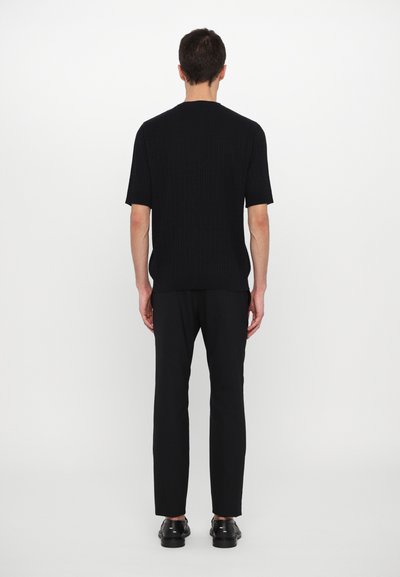 Camisa negra de manga corta con canalé vista desde la parte posterior, combinada con pantalones ajustados negros y zapatos negros. Textura suave, diseño ajustado.