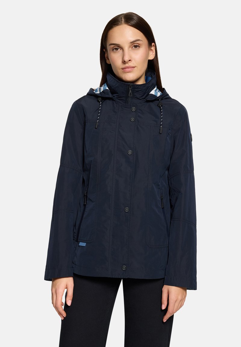 Granatowa wodoodporna kurtka, z kapturem wyściełanym niebiesko-białą kratką, zatrzaskami i dwoma bocznymi kieszeniami. Gładka tekstura.