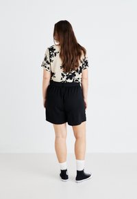 Pantalones cortos negros con una cinturilla elástica combinados con una blusa beige que presenta un patrón floral negro. Se llevan con zapatillas altas negras y calcetines blancos.