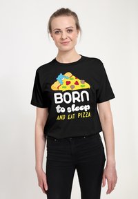 Camiseta negra con un gráfico colorido de una porción de pizza con un oso, el texto dice "NACIDO para dormir Y comer PIZZA" en fuentes juguetonas.