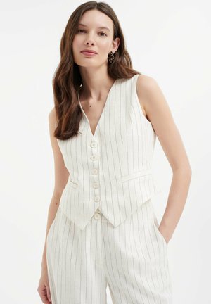 Chaleco blanco a rayas con escote en V, botones frontales y bolsillos. Fabricado en tela ligera, con un diseño ajustado y dobladillo en ángulo.