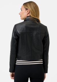 Zwarte leren jas met een cropped ontwerp, voorzien van een gestreepte gebreide tailleband en subtiele stikdetails. Glad materiaal met een strakke afwerking.