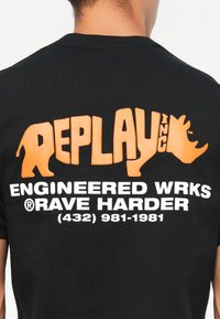 Sort bomulds t-shirt med orange og hvid grafisk tekst. Designet inkluderer brandnavnet "REPLAY INC," en bjørnesilhuet og kontaktoplysninger.
