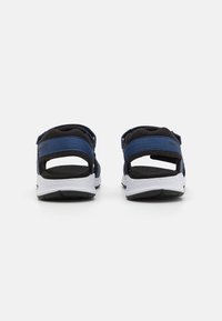 Svart och blå sandal med tygremmar och en vit gummisula. Öppen design baktill med justerbara remmar för en perfekt passform.