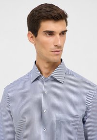 Camicia a maniche corte con bottoni in stripes verticali blu e bianche, caratterizzata da un colletto classico e una singola tasca sul petto. Tessuto dalla consistenza liscia.