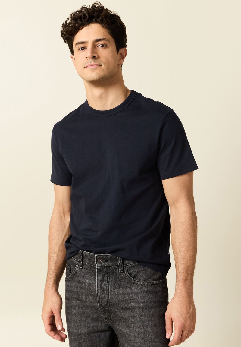 T-shirt in cotone blu navy con maniche corte e collo a giro, abbinato a jeans in denim grigio scuro; texture liscia, design semplice.