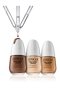 Tre flasker med Clinique Even Better Clinical Serum Foundation i forskjellige nyanser: mørkebrun, lys beige og mellombeige. Klar dryppere over.
