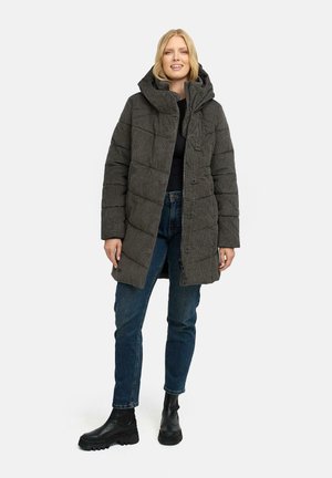 Grijze pufferjas met grote capuchon, gevoerd patroon, knopen aan de voorkant en zijzakken. G gedragen over een zwarte top met blauwe jeans en zwarte laarzen.