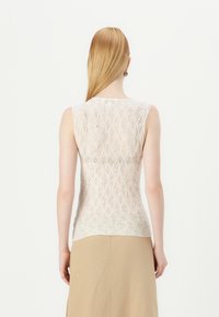 Hedvábný bezramínkový top v off-white barvě s diamantovým vzorem, průhlednou strukturou, kulatým výstřihem a o něco delším zadu. Spárováno s béžovou sukní.